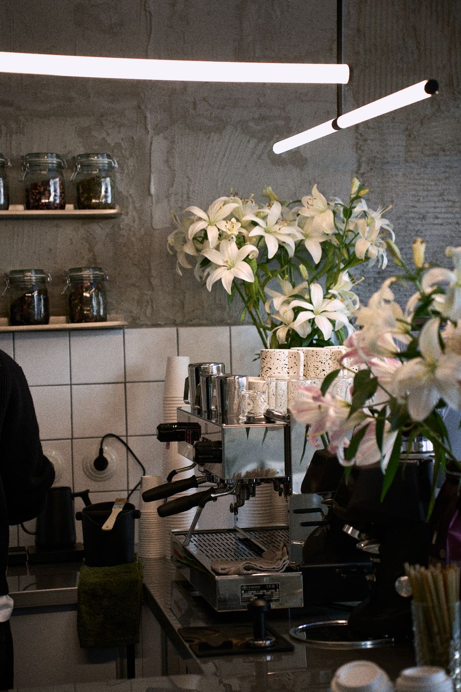 Bar Bruk Cafe: ekspres, lampy liniowe i kwiaty na tle betonowej ściany